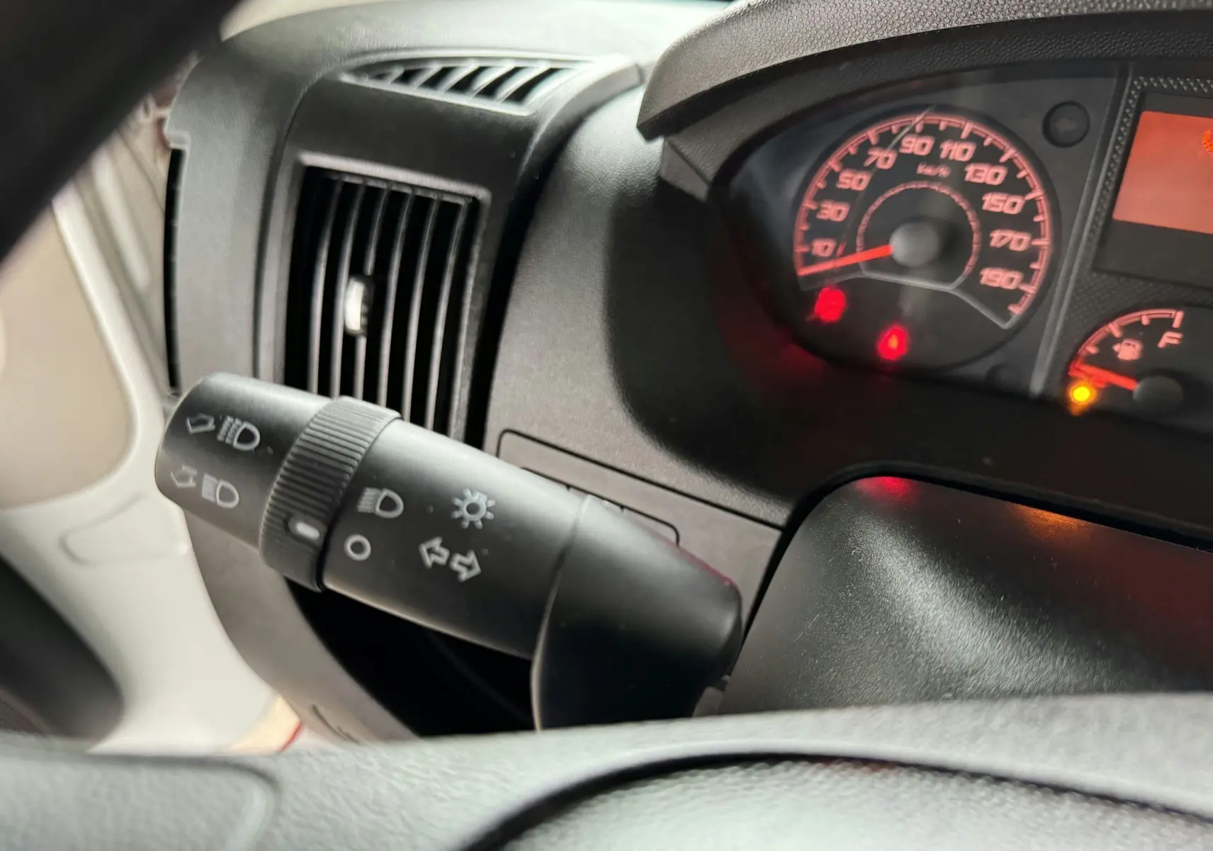 Gros plan sur le commodo des feux et le tableau de bord éclairé du Citroën Jumper Benne rouge, intérieur noir.