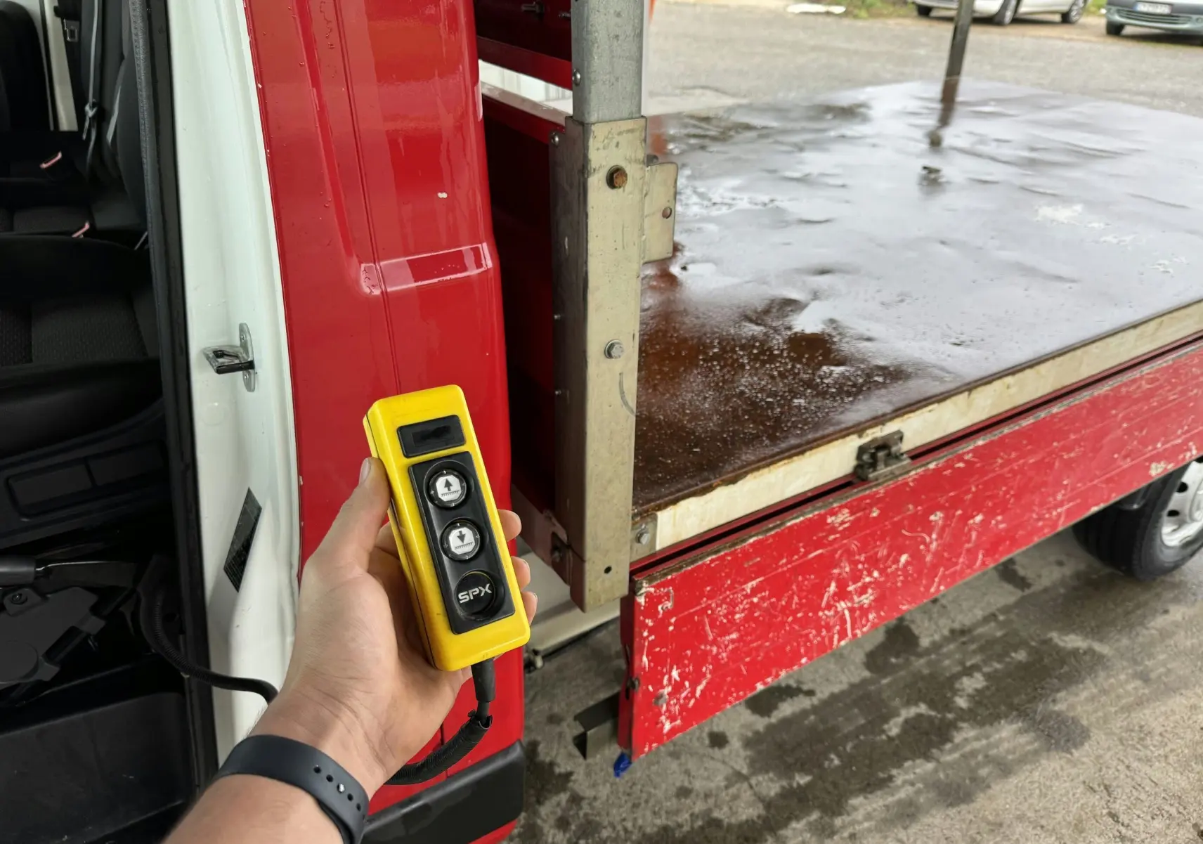 Télécommande jaune tenue devant la benne rouge arrière droite ouverte d'un Citroën Jumper Châssis Cabine de 2019.