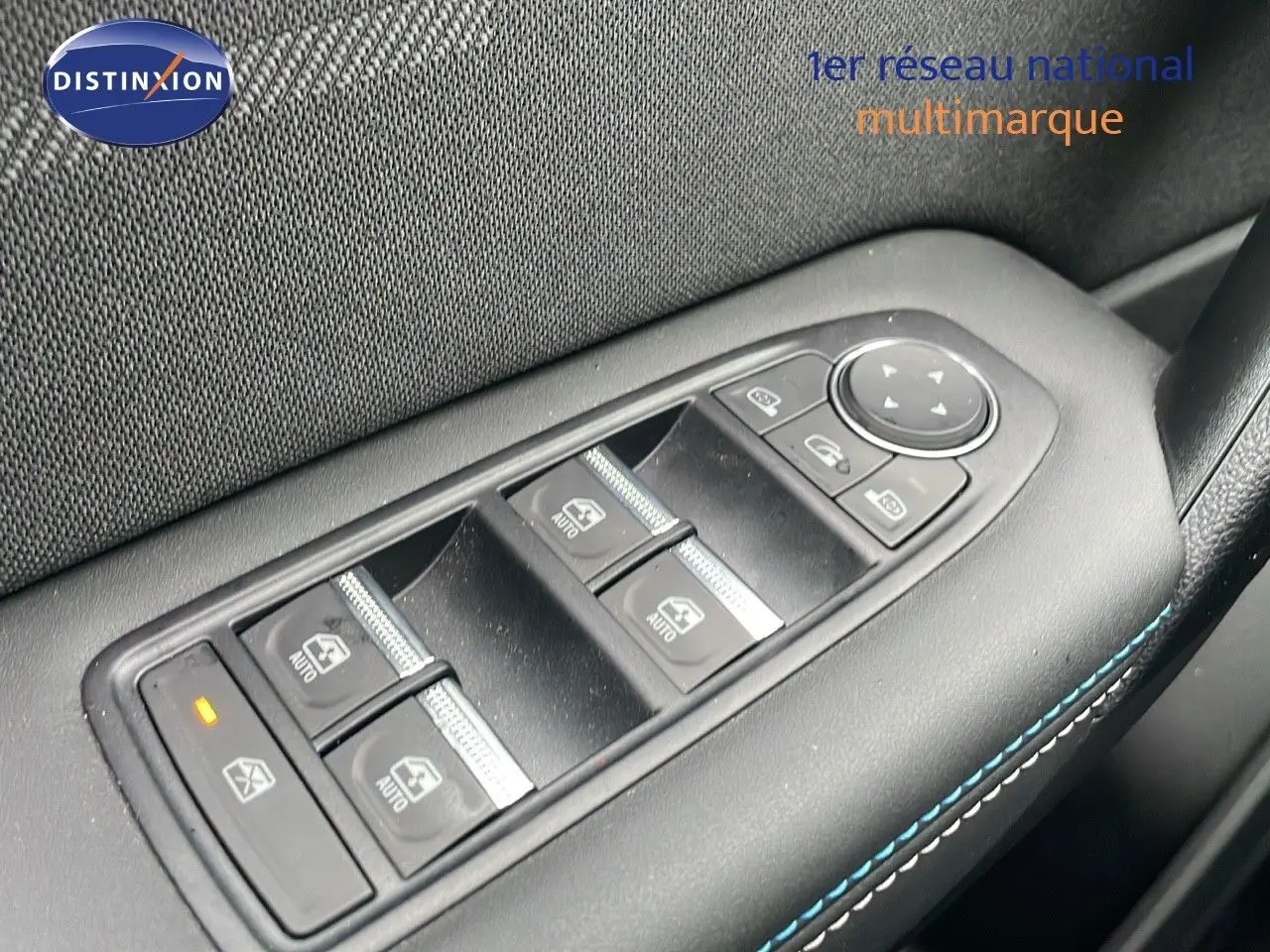 Gros plan sur les commandes des vitres électriques côté conducteur du Renault Symbioz gris Rafale métal, avec surpiqûres bleues.