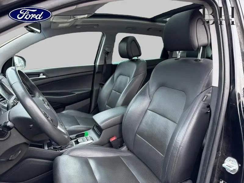 Intérieur avant noir du Hyundai Tucson 2018, vue côté conducteur avec sièges cuir et toit ouvrant panoramique.