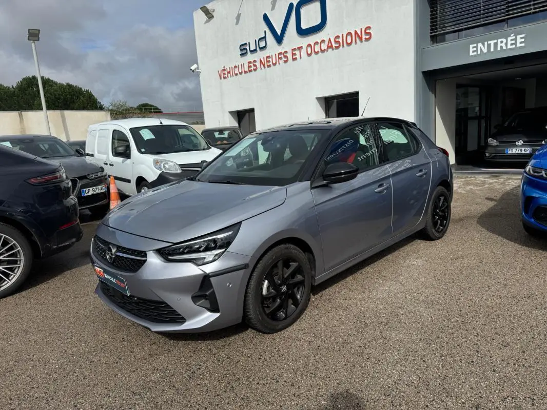 Opel Corsa 1.2 Turbo gris clair vue 3/4 avant droit avec jantes noires, stationnée devant un concessionnaire.