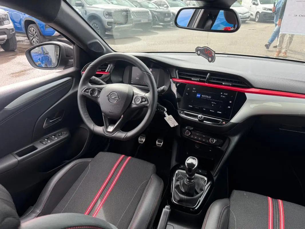 Vue intérieure côté conducteur de l’Opel Corsa gris clair 2022, avec volant, tableau de bord et sièges noirs à bandes rouges.