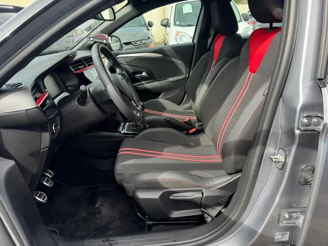 Vue intérieure côté conducteur de l’Opel Corsa gris clair 2022, sièges noirs avec surpiqûres rouges et volant multifonction.