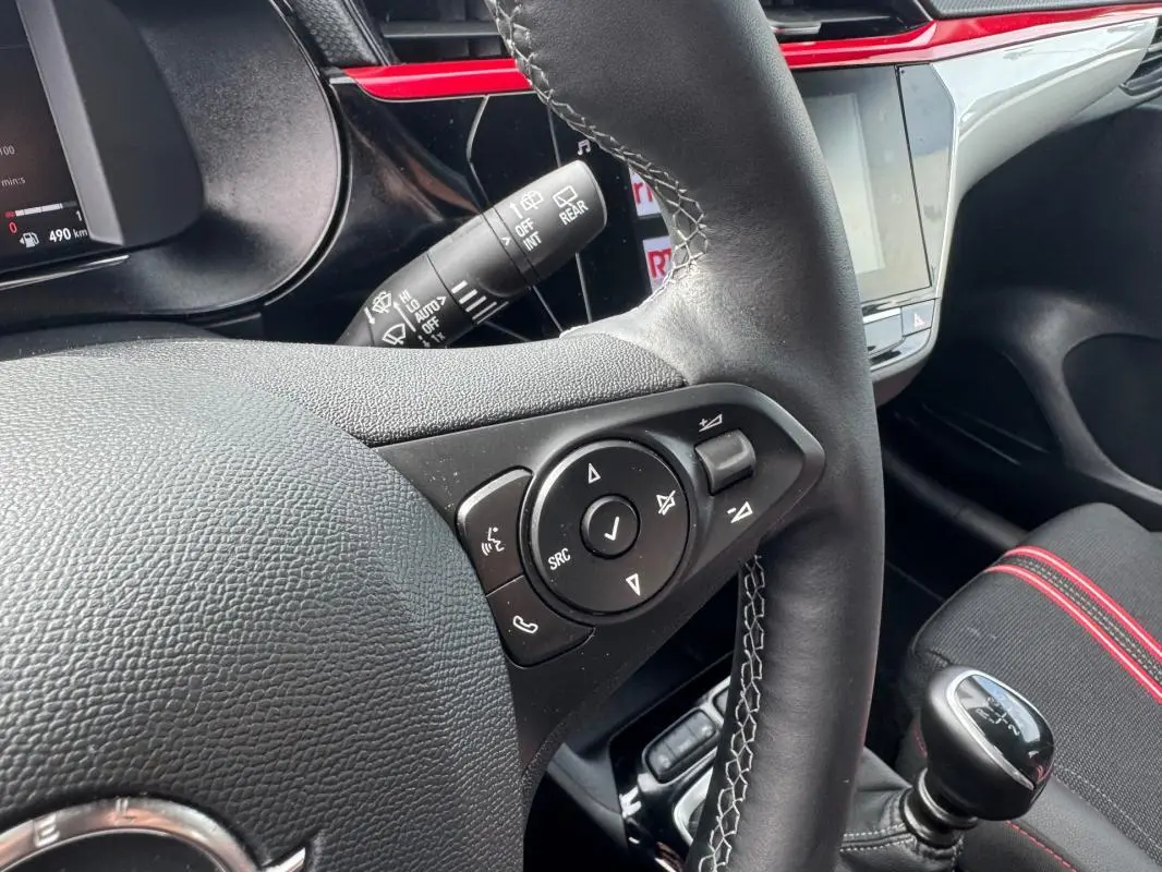 Gros plan sur le volant et levier de vitesse manuel de l’Opel Corsa gris clair 2022 avec surpiqûres blanches et détails rouges intérieurs.