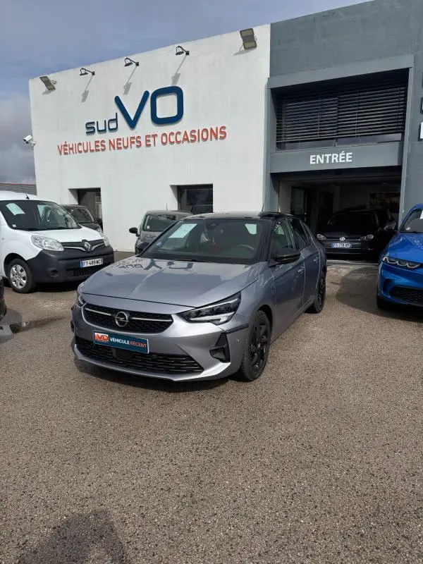 Opel Corsa gris clair 2022 en 3/4 avant droit, finition GS Line avec jantes noires, devant un garage Sud VO.