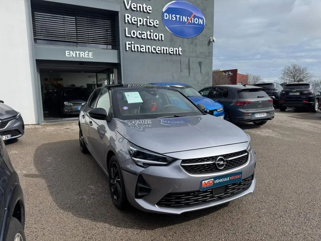 Opel Corsa gris clair vue 3/4 avant droit, calandre noire et jantes foncées, devant un garage Distinxion.