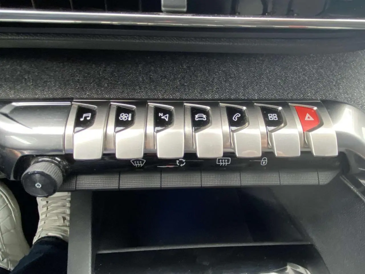 Gros plan sur la rangée de boutons argentés et rouges de la console centrale d’un Peugeot 3008 blanc, intérieur noir.