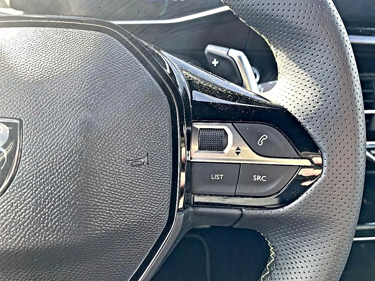 Gros plan sur le volant cuir perforé de la Peugeot 2008 1.2 hybrid 145 GT, avec commandes multifonctions à droite.