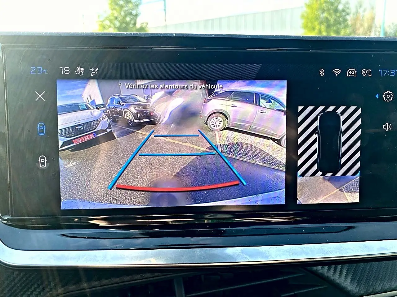 Écran tactile montrant la caméra de recul d'une Peugeot 2008 noire, avec guidage de trajectoire en bleu et rouge.