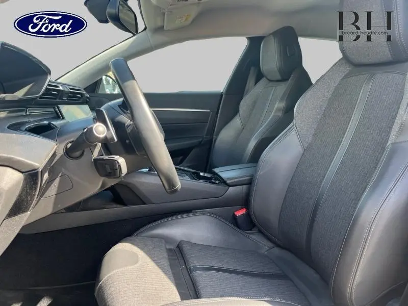Vue intérieure côté conducteur de la Peugeot 508 SW 2021 avec sièges en tissu et cuir gris, volant cuir et console centrale noire.