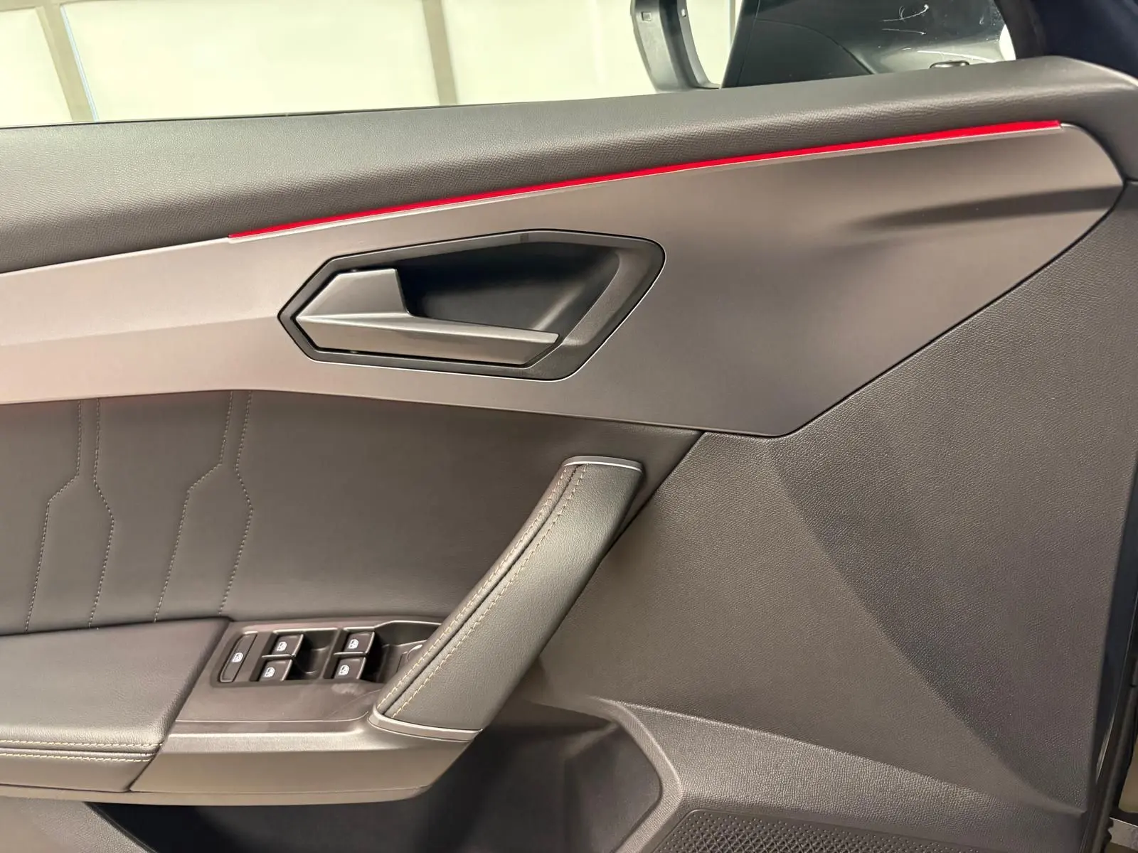 Gros plan sur la porte intérieure côté gauche du CUPRA Formentor 2023 avec surpiqûres et bande lumineuse rouge.