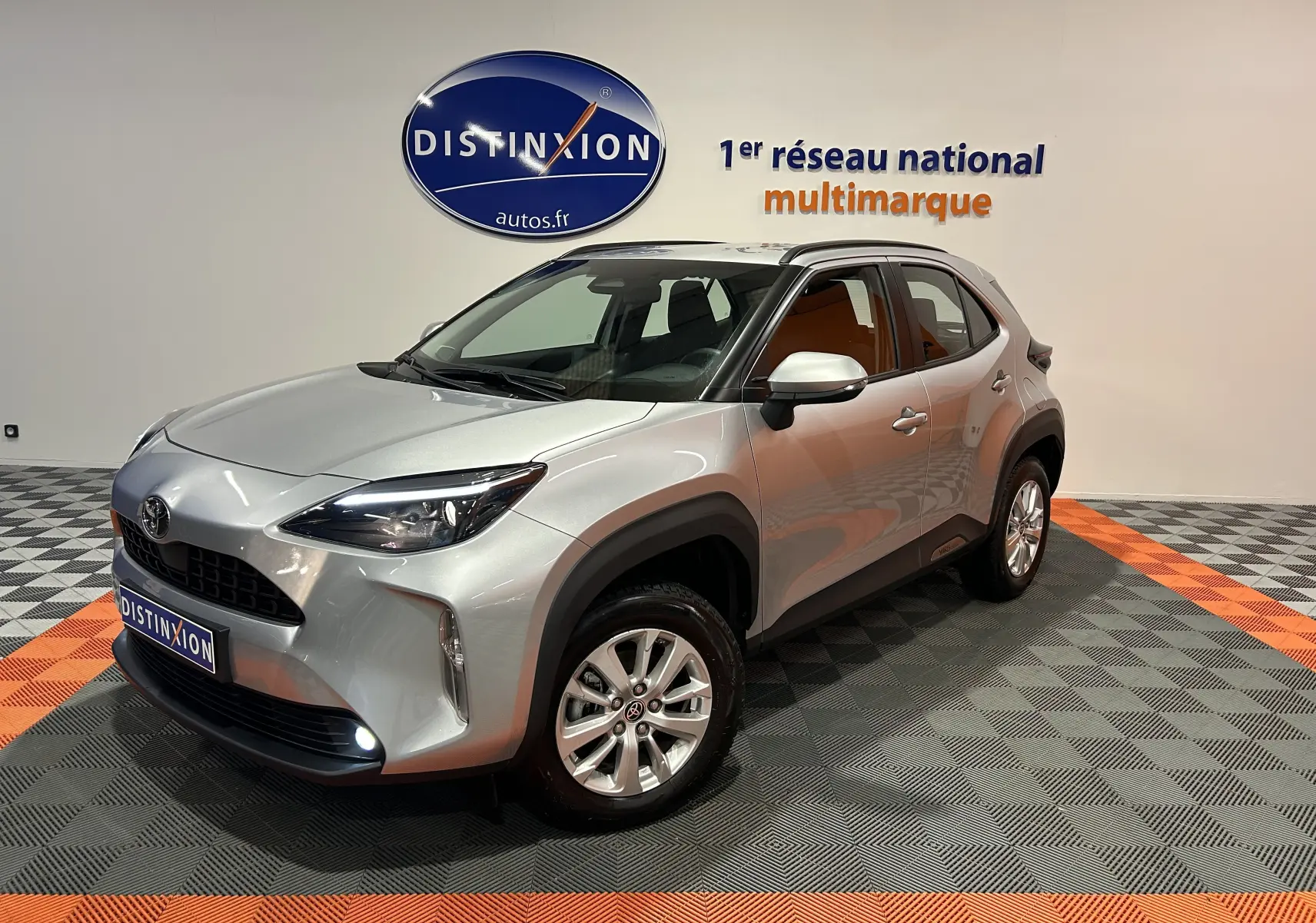 Toyota Yaris Cross gris minéral vue 3/4 avant droit en intérieur avec jantes alliage et feux allumés.