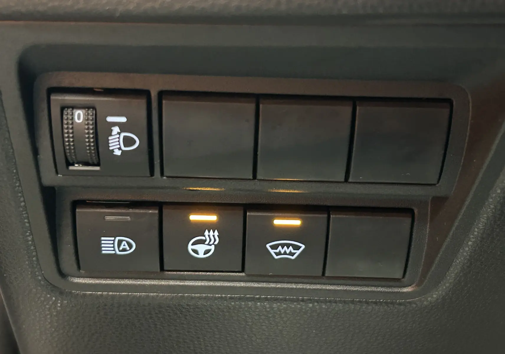 Gros plan sur les boutons de commande du volant chauffant et pare-brise chauffant dans une Toyota Yaris Cross gris minéral.