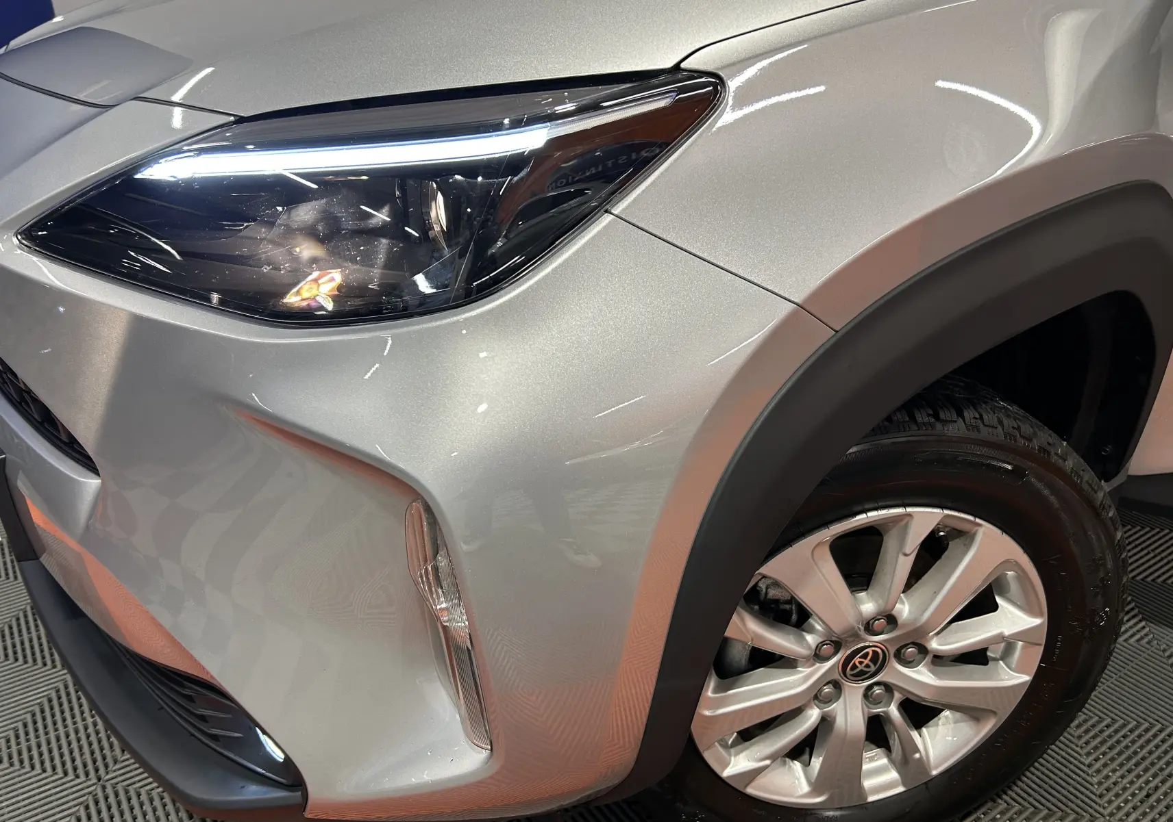 Gros plan sur l'avant droit gris minéral du Toyota Yaris Cross 116h avec phare LED allumé et jante alliage visible.