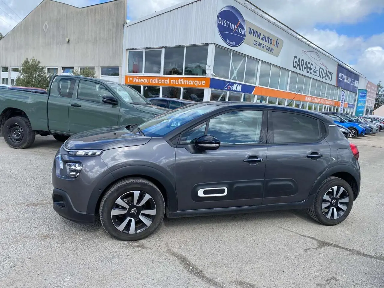 Profil droit d'une Citroën C3 gris platinium 2021 avec Airbump blanc et toit noir, stationnée devant un garage.