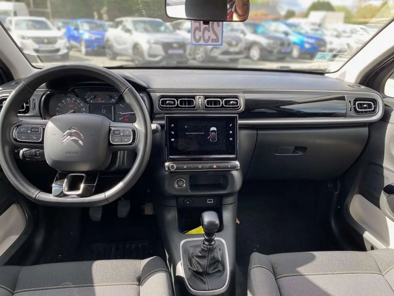 Vue intérieure avant du poste de conduite de la Citroën C3 2021, tableau de bord noir avec écran tactile central et volant multifonction.