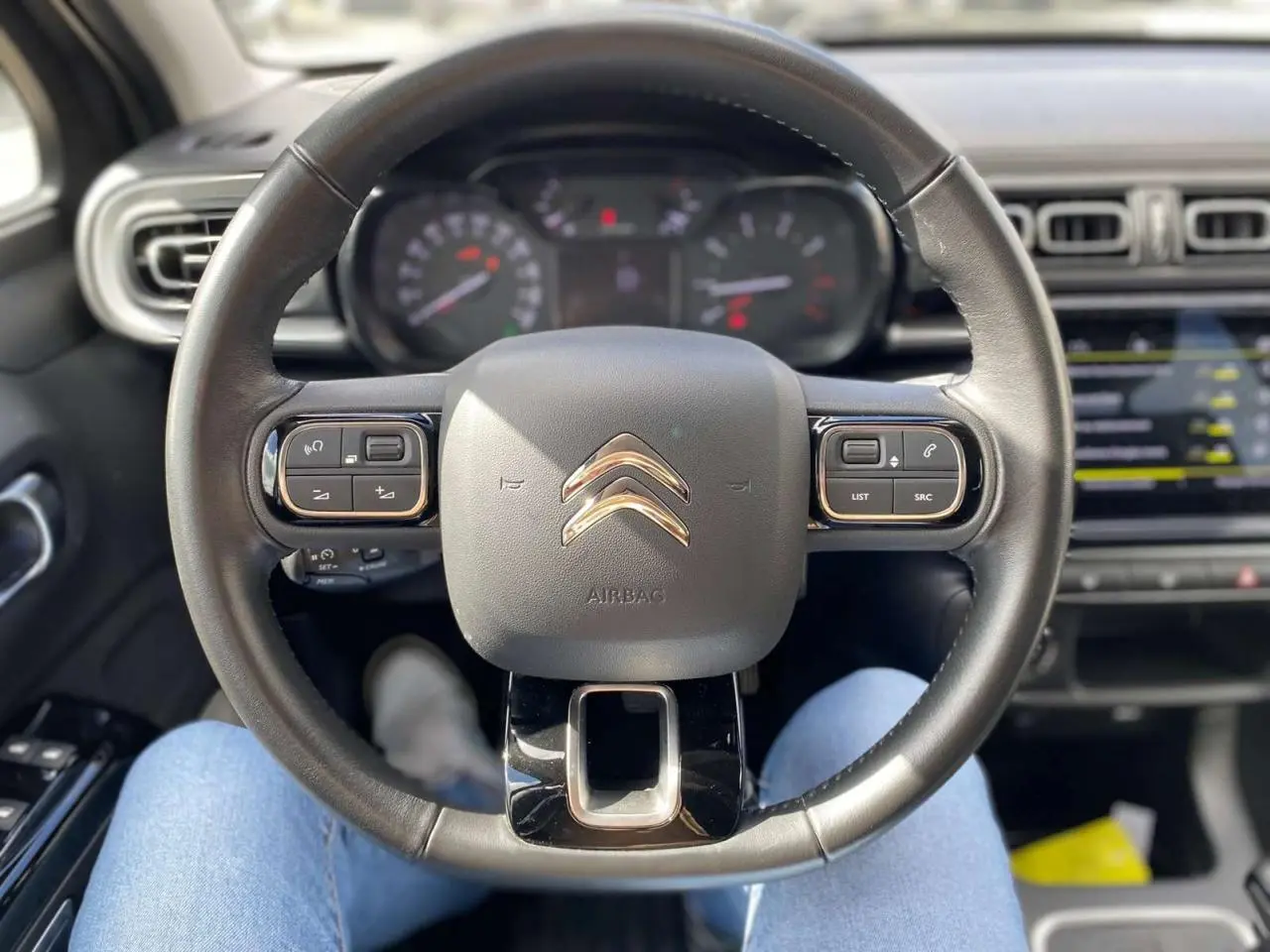 Vue centrée sur le volant noir de la Citroën C3 2021 avec tableau de bord et écran tactile en arrière-plan flou.