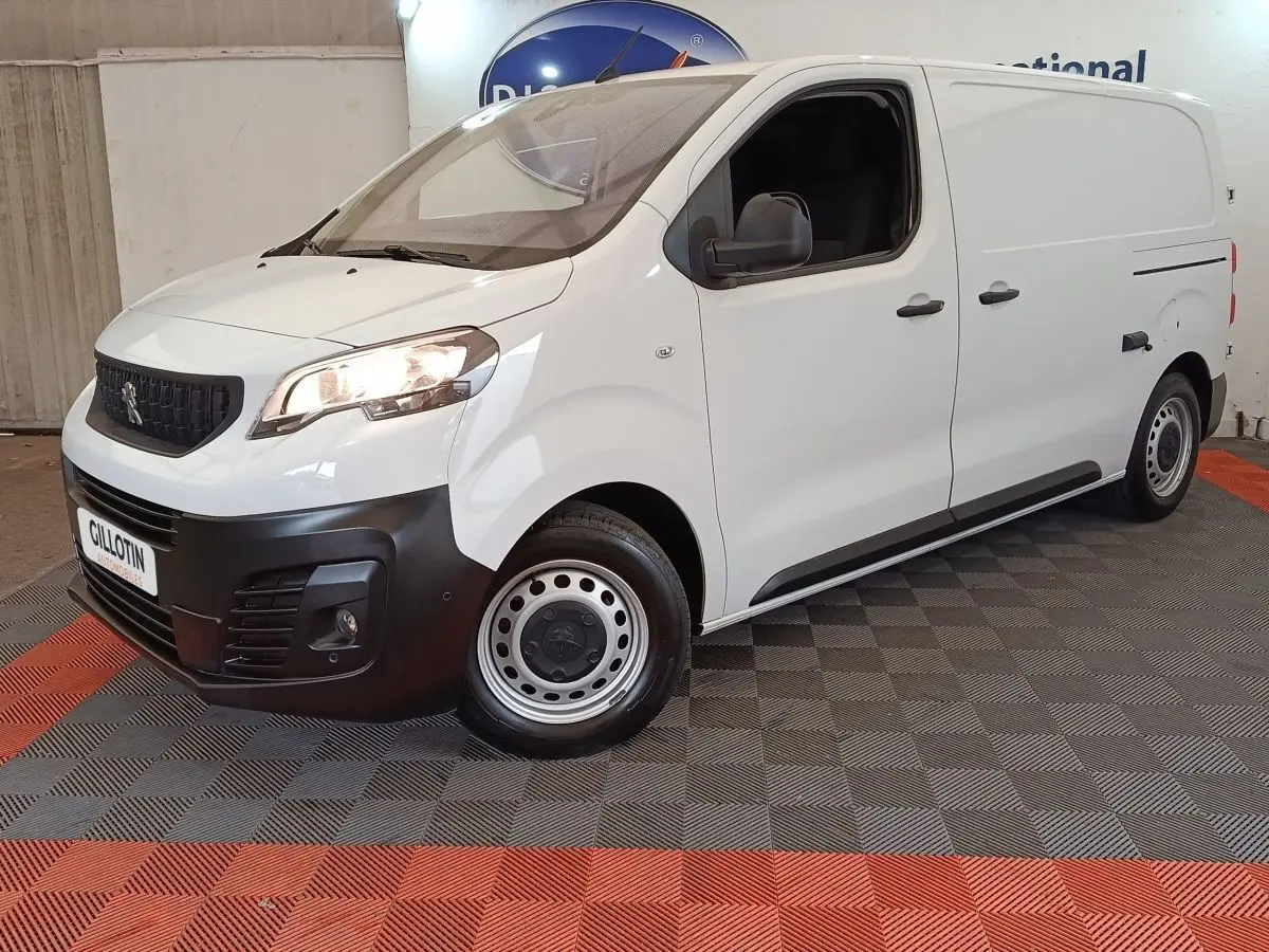 Vue 3/4 avant droit d’un Peugeot Expert Fourgon blanc avec pare-chocs noir et jantes acier, stationné en intérieur.