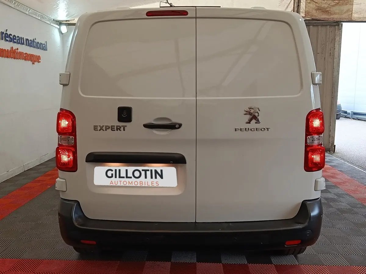 Vue arrière du Peugeot Expert Fourgon blanc 2023 avec portes battantes et feux arrière allumés en intérieur showroom.