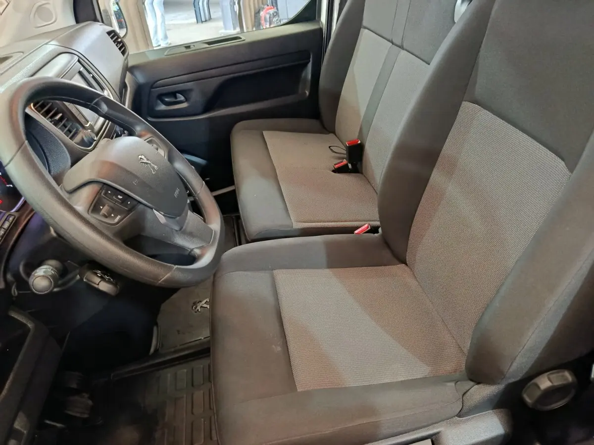 Vue intérieure côté conducteur du Peugeot Expert Fourgon 2023, sièges tissu gris et volant multifonctions noir.
