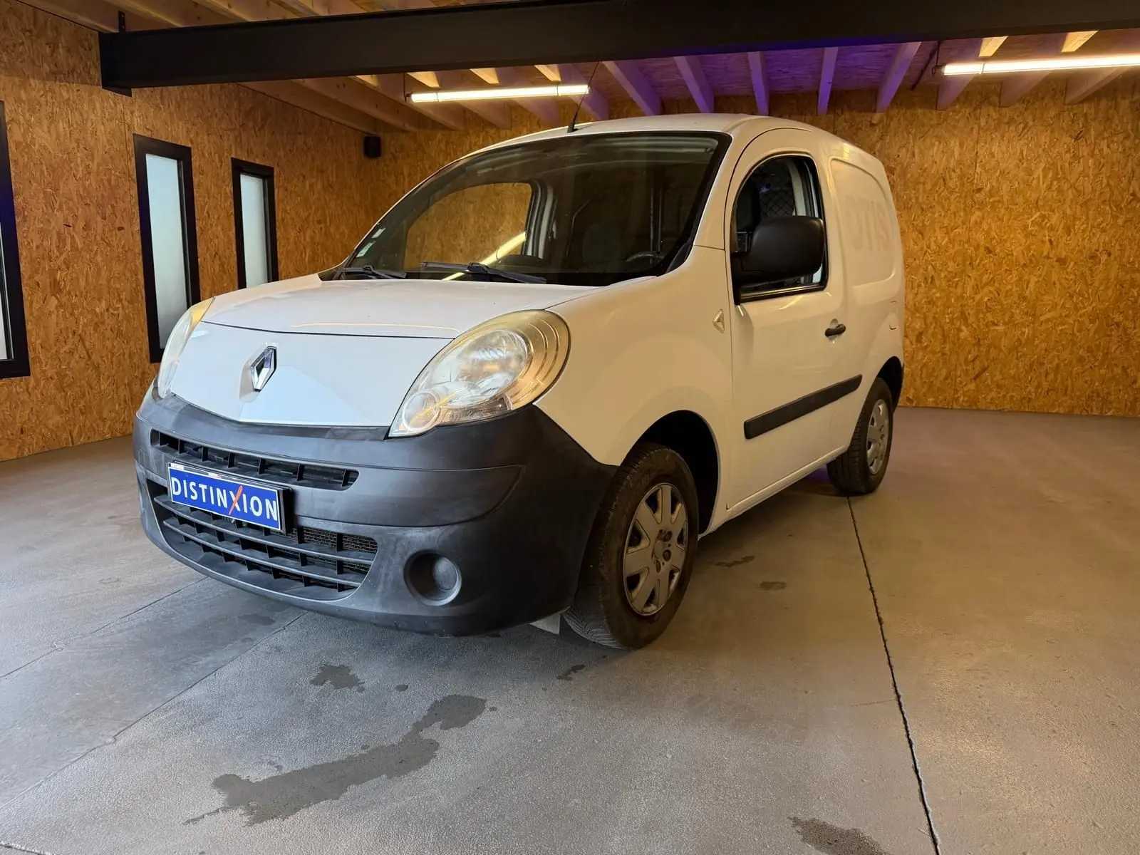 Renault Kangoo blanc 2011 en 3/4 avant droit, avec pare-chocs noir mat et plaque Distinxion visible.
