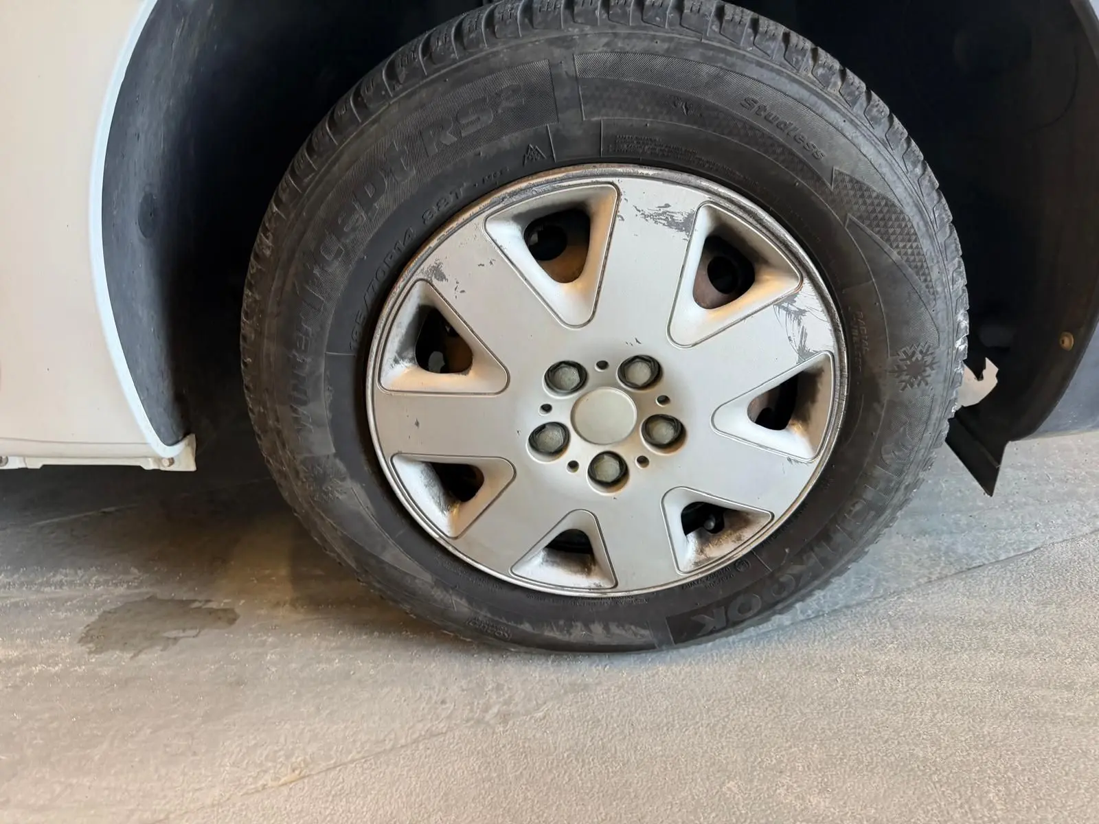 Gros plan sur la roue avant gauche d’un Renault Kangoo blanc de 2011, avec jante en acier et enjoliveur usé.