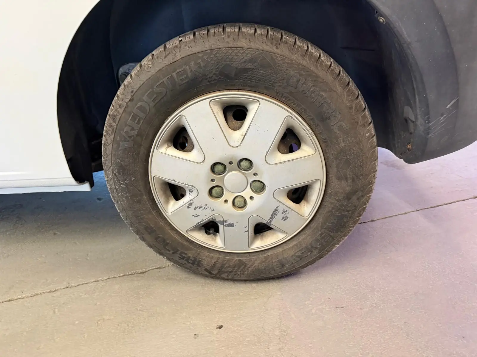 Gros plan sur la roue avant droite d’un Renault Kangoo blanc de 2011, jante avec traces d’usure visibles.