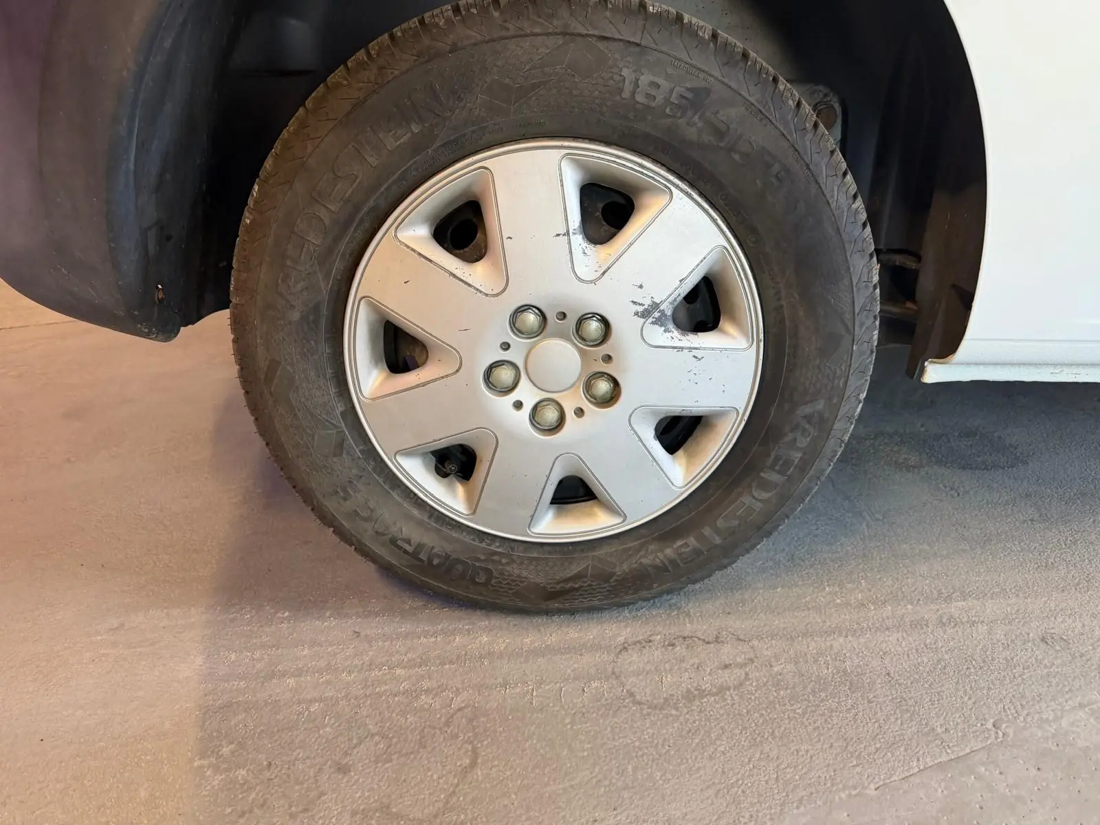 Gros plan sur la roue avant droite d’un Renault Kangoo blanc de 2011, montrant la jante en alliage avec quelques rayures.