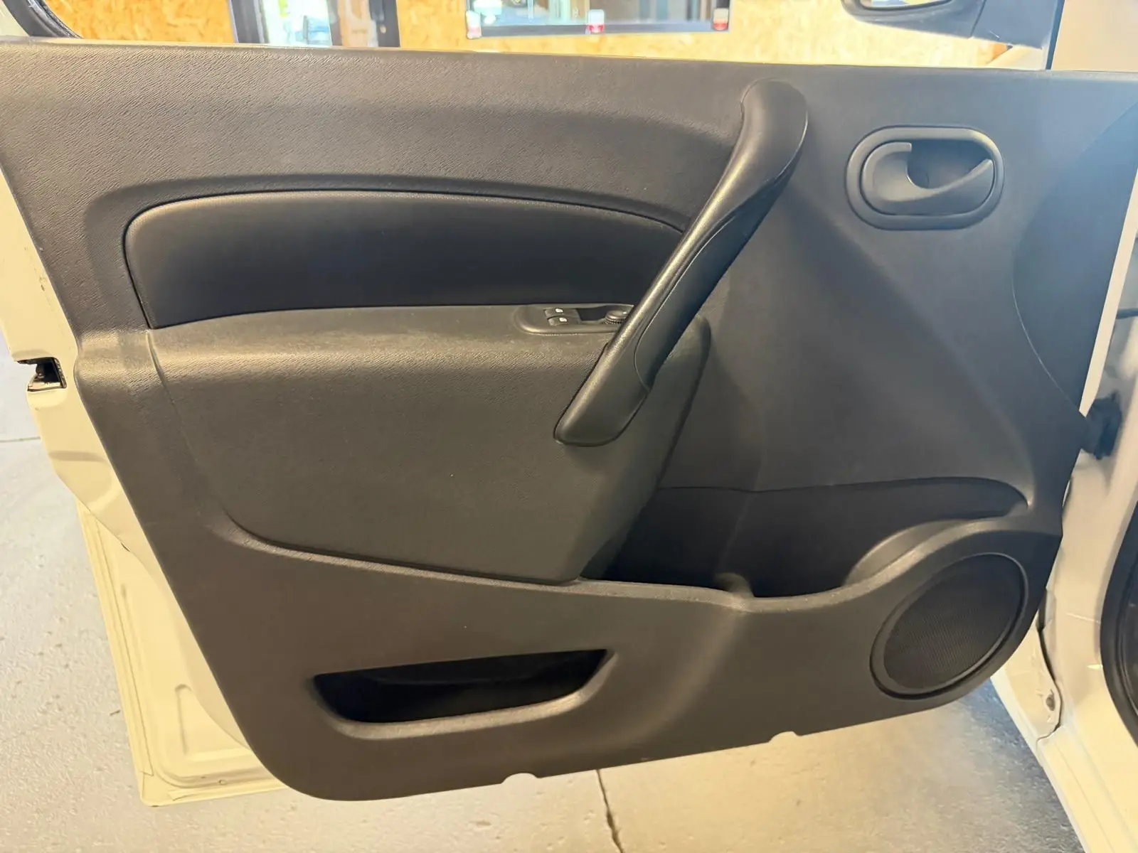 Vue intérieure de la porte avant gauche noire du Renault Kangoo blanc 2011, avec poignée et haut-parleur intégrés.