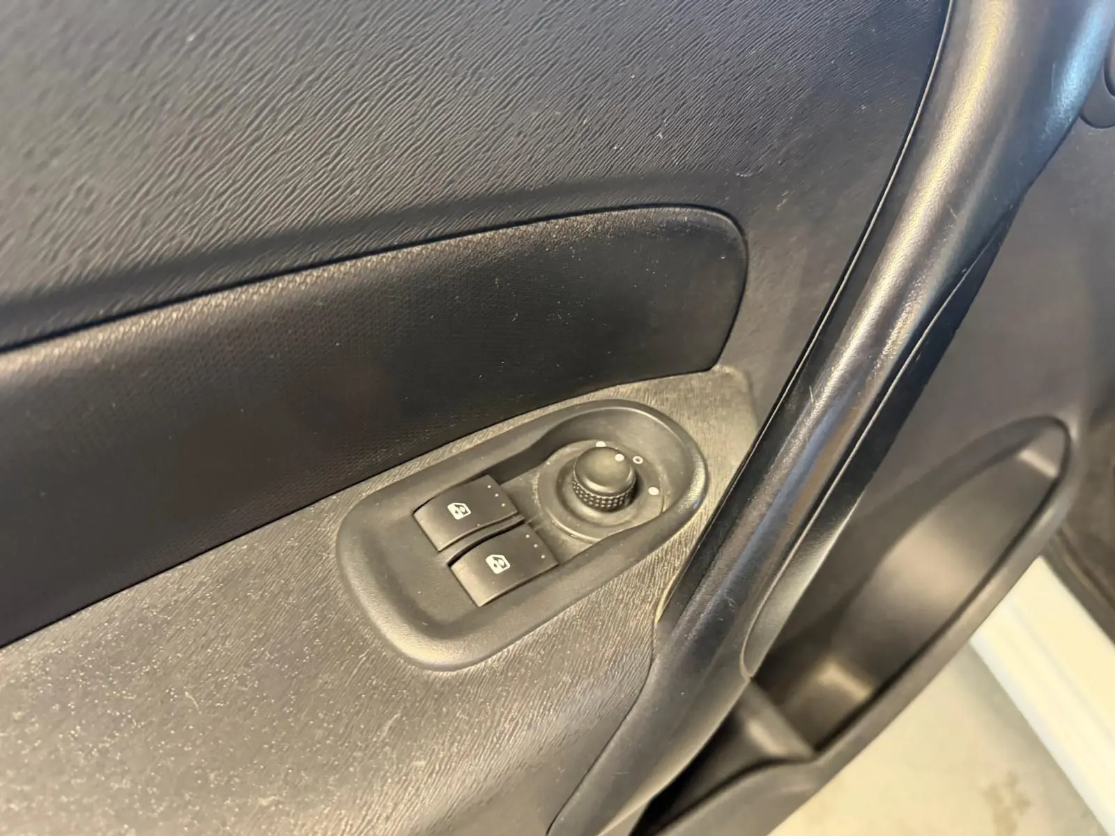 Gros plan sur la commande des vitres électriques côté conducteur du Renault Kangoo blanc de 2011, intérieur noir.