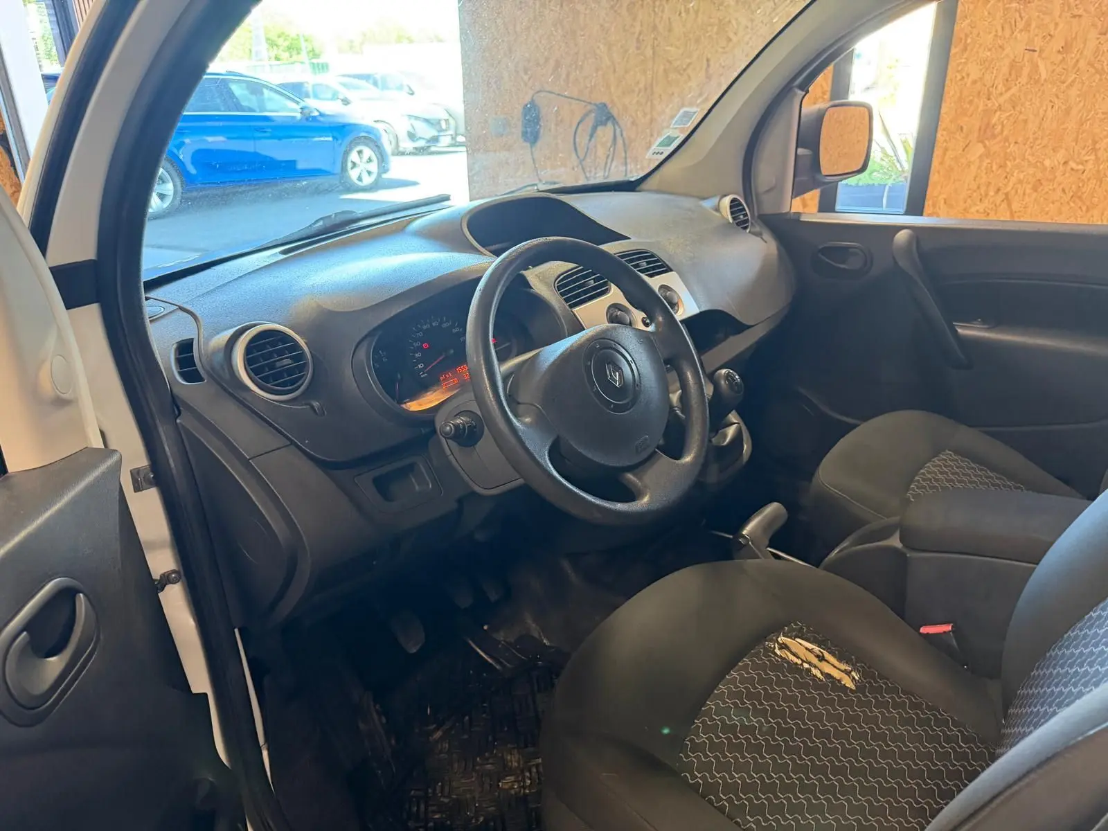 Vue intérieure côté conducteur du Renault Kangoo 1.5 DCI blanc, montrant le tableau de bord et les sièges en tissu noir.