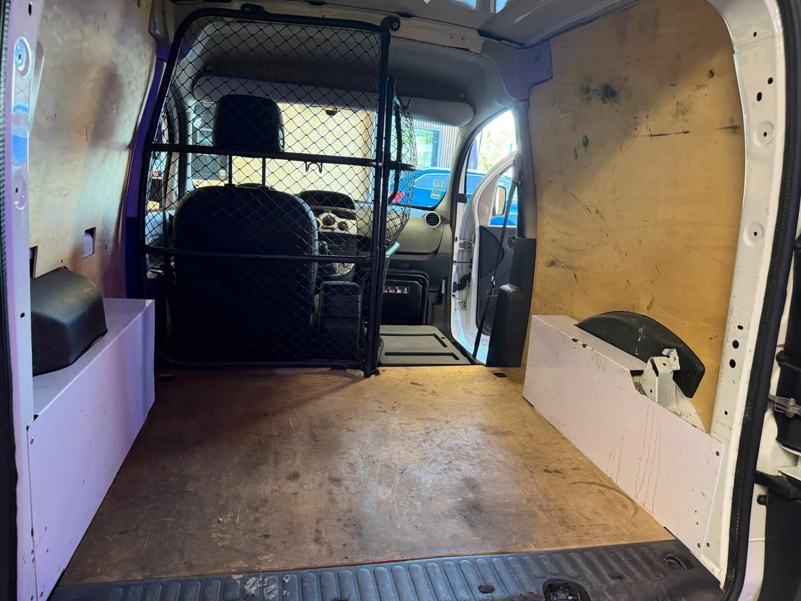 Vue intérieure arrière du Renault Kangoo blanc 2011, montrant l'espace de chargement avec cloison métallique et parois en bois.