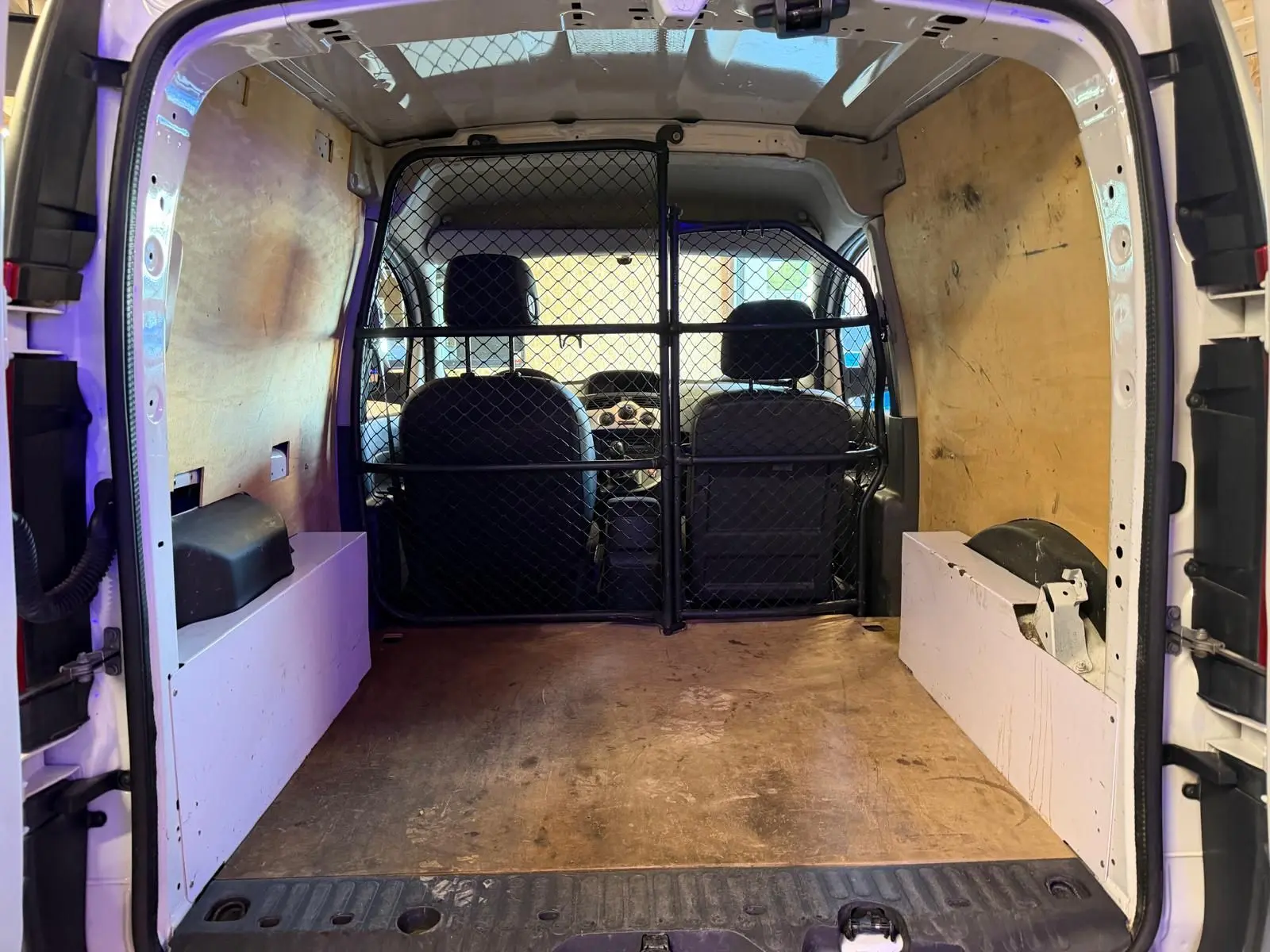 Vue intérieure arrière du Renault Kangoo blanc 2011, montrant l'espace de chargement avec cloison métallique et revêtement bois.