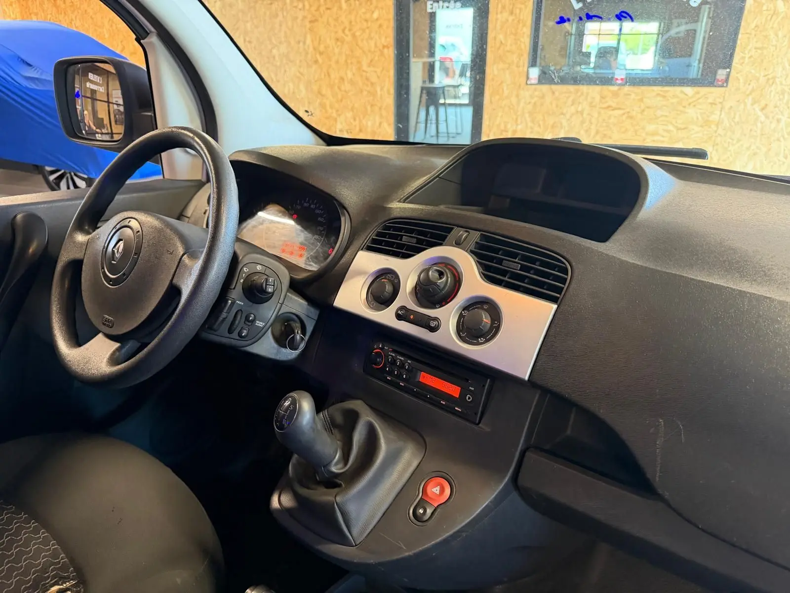 Vue intérieure côté conducteur du tableau de bord noir et volant d’un Renault Kangoo blanc avec levier de vitesse manuel.
