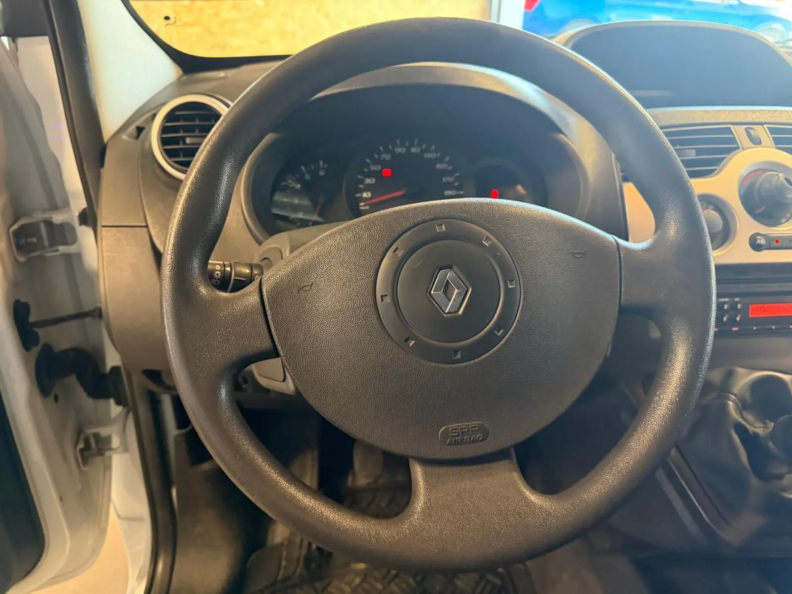 Vue intérieure centrée sur le volant noir du Renault Kangoo blanc 2011 avec tableau de bord et levier de vitesse manuel visibles.