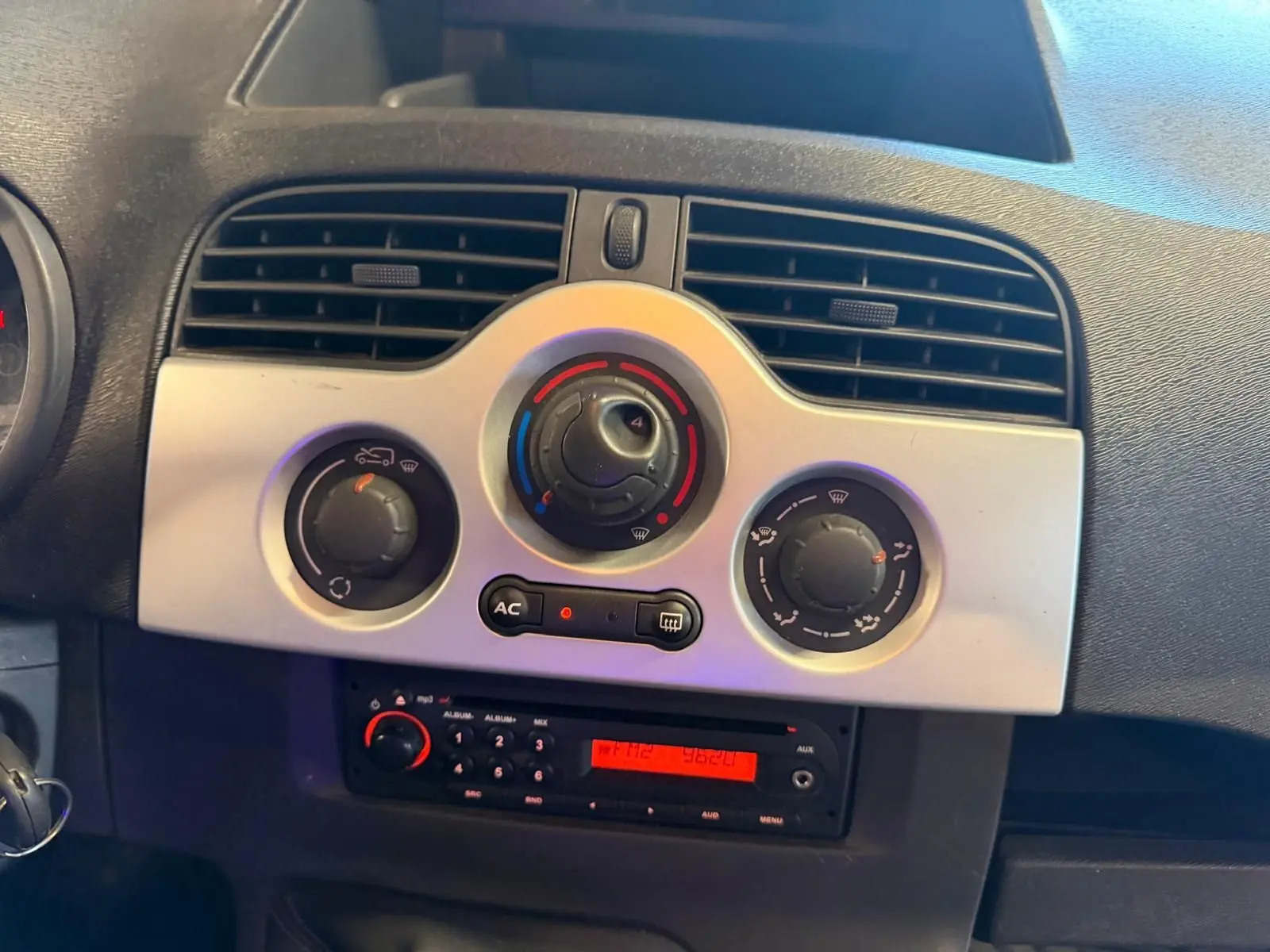 Tableau de bord intérieur du Renault Kangoo 2011, vue centrée sur les commandes de climatisation et la radio avec éclairage rouge.