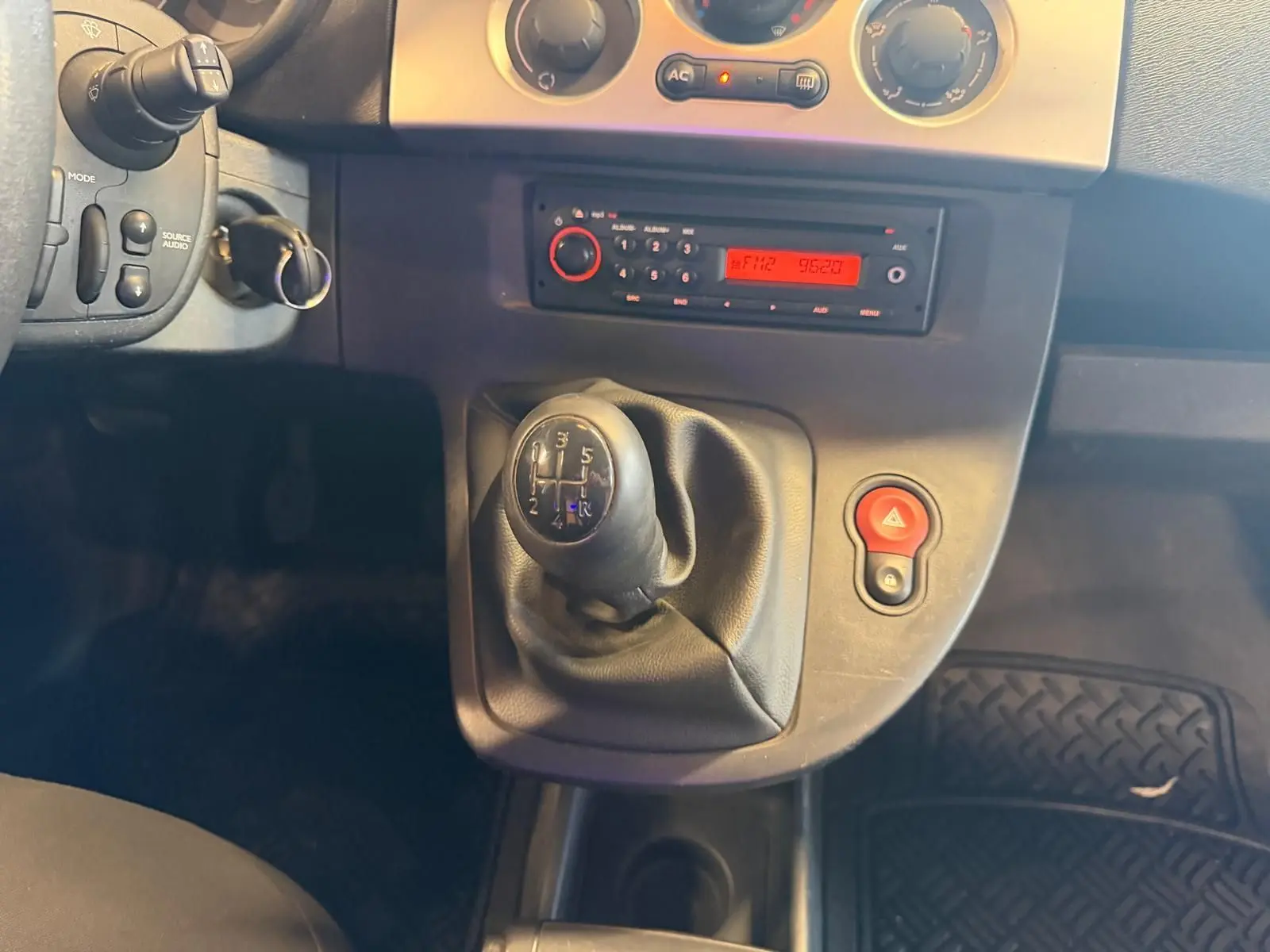 Gros plan sur le levier de vitesse manuel et la console centrale du Renault Kangoo blanc, avec radio et bouton de warning rouge.