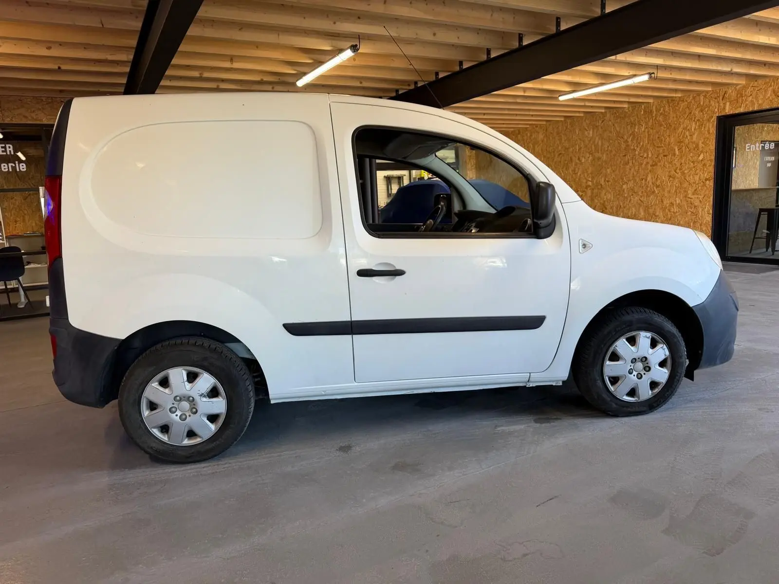 Profil côté gauche d’un Renault Kangoo blanc 2011, version utilitaire compacte avec portes pleines et jantes acier.