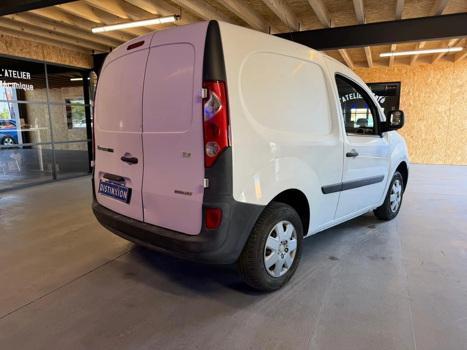 Renault Kangoo blanc vue 3/4 arrière droit dans un garage avec portes arrière fermées et pare-chocs noirs.