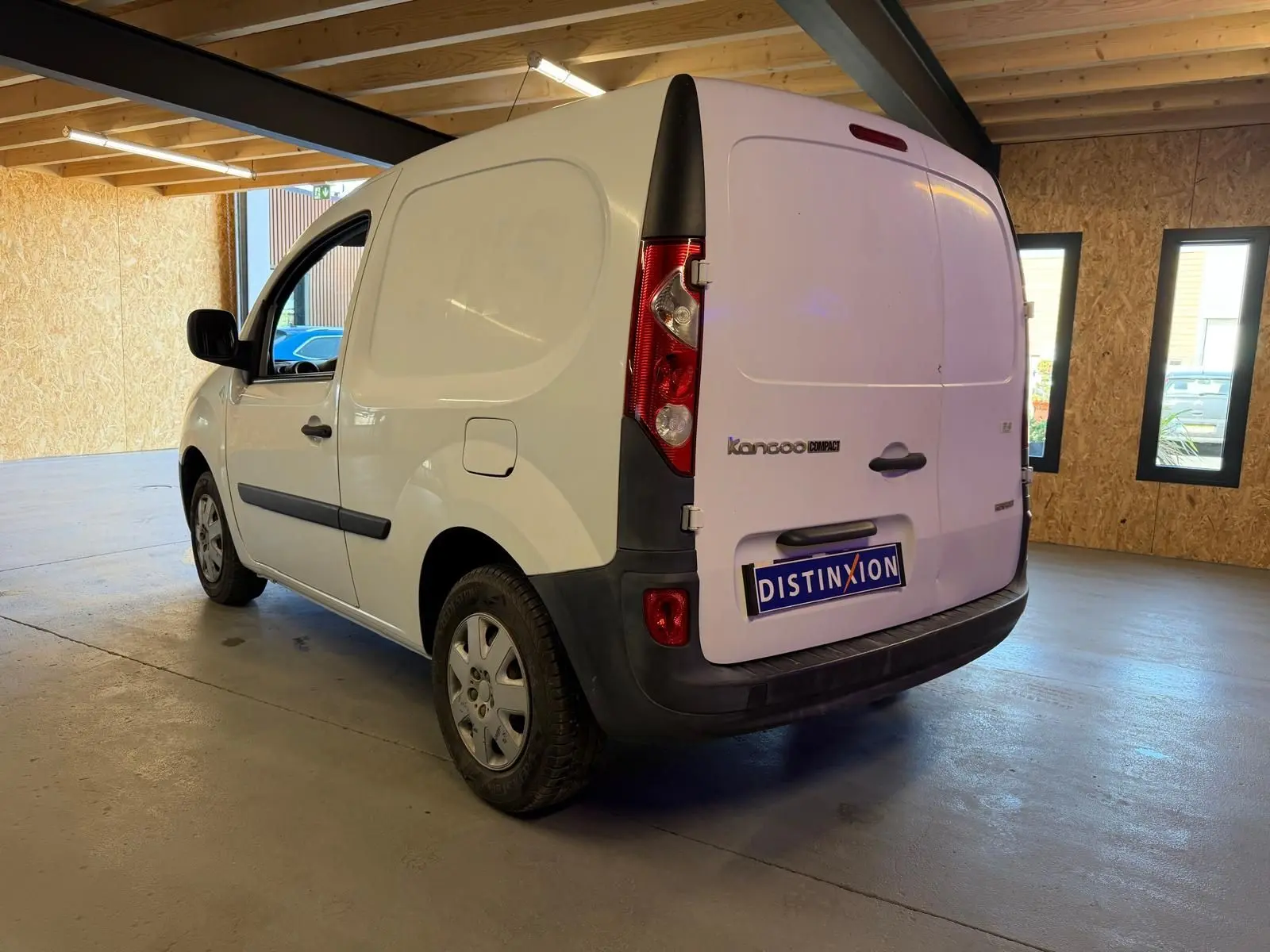 Vue 3/4 arrière droite d'un Renault Kangoo blanc 2011 version Compact, utilitaire avec portes arrière pleines en intérieur d'entrepôt.