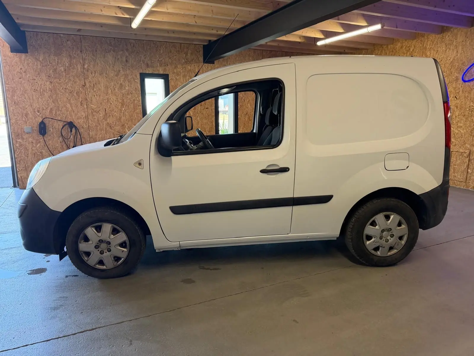 Vue de profil côté gauche d’un utilitaire Renault Kangoo blanc 2011 avec porte latérale pleine, stationné en intérieur.
