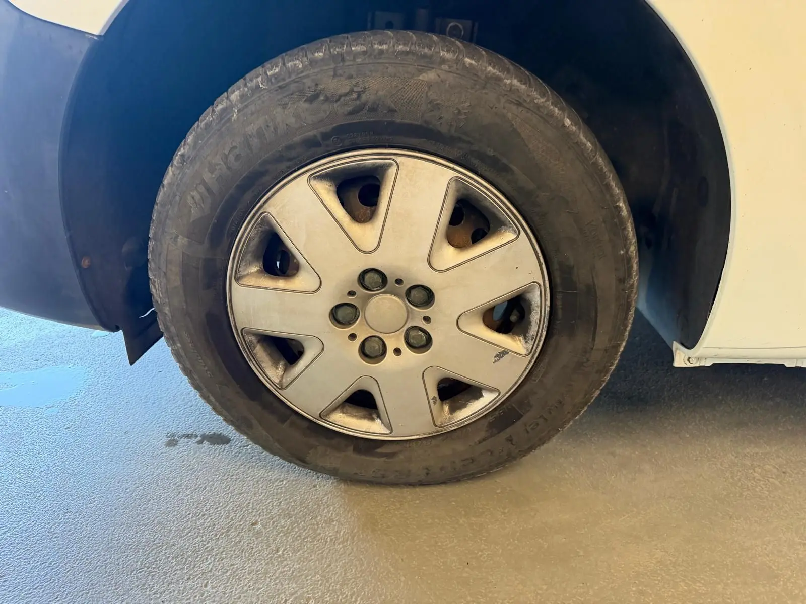 Gros plan sur la roue avant gauche d'un Renault Kangoo blanc de 2011, avec jante en alliage et pneu usé.