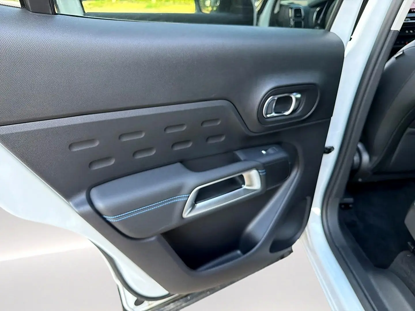 Vue rapprochée de la porte arrière gauche noire avec surpiqûres bleues sur un Citroën C5 Aircross blanc 2025.