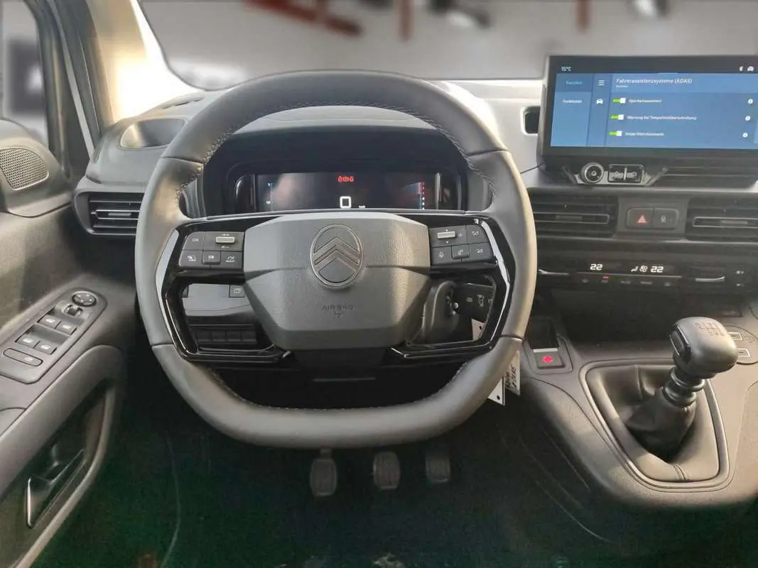 Vue intérieure centrée sur le volant cuir multifonctions et levier de vitesse manuel du Citroën Berlingo gris Artense.