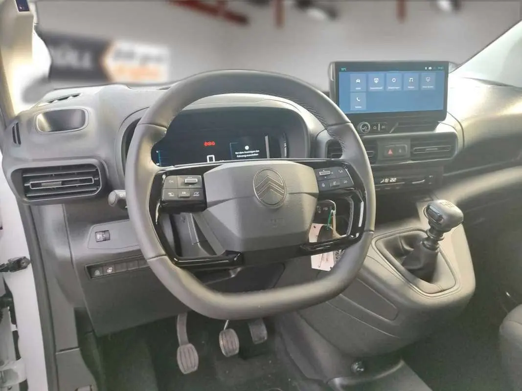 Vue intérieure centrée sur le volant cuir multifonctions et la console avec écran tactile du Citroën Berlingo gris Artense.