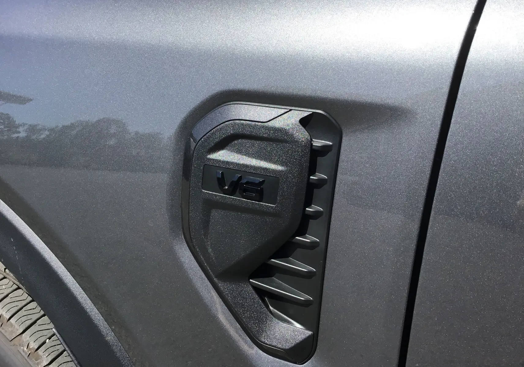 Gros plan sur la prise d'air latérale gris carbone du Ford Ranger Wildtrak avec logo V6 en relief.