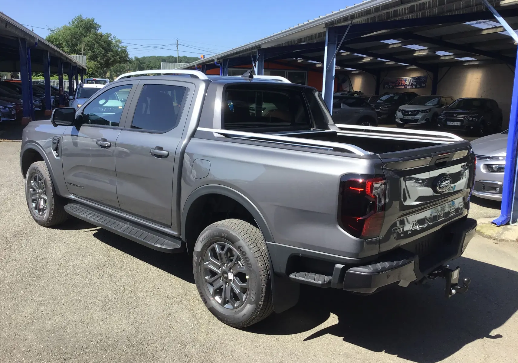 Ford Ranger Double Cabine gris carbone vu en 3/4 arrière droit, avec rideau de plateau électrique et attelage visible.