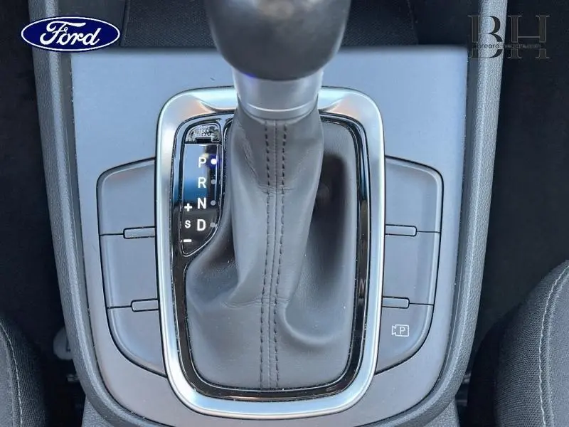 Le levier de vitesses automatique en cuir noir vu de dessus, entouré de commandes sur console grise.