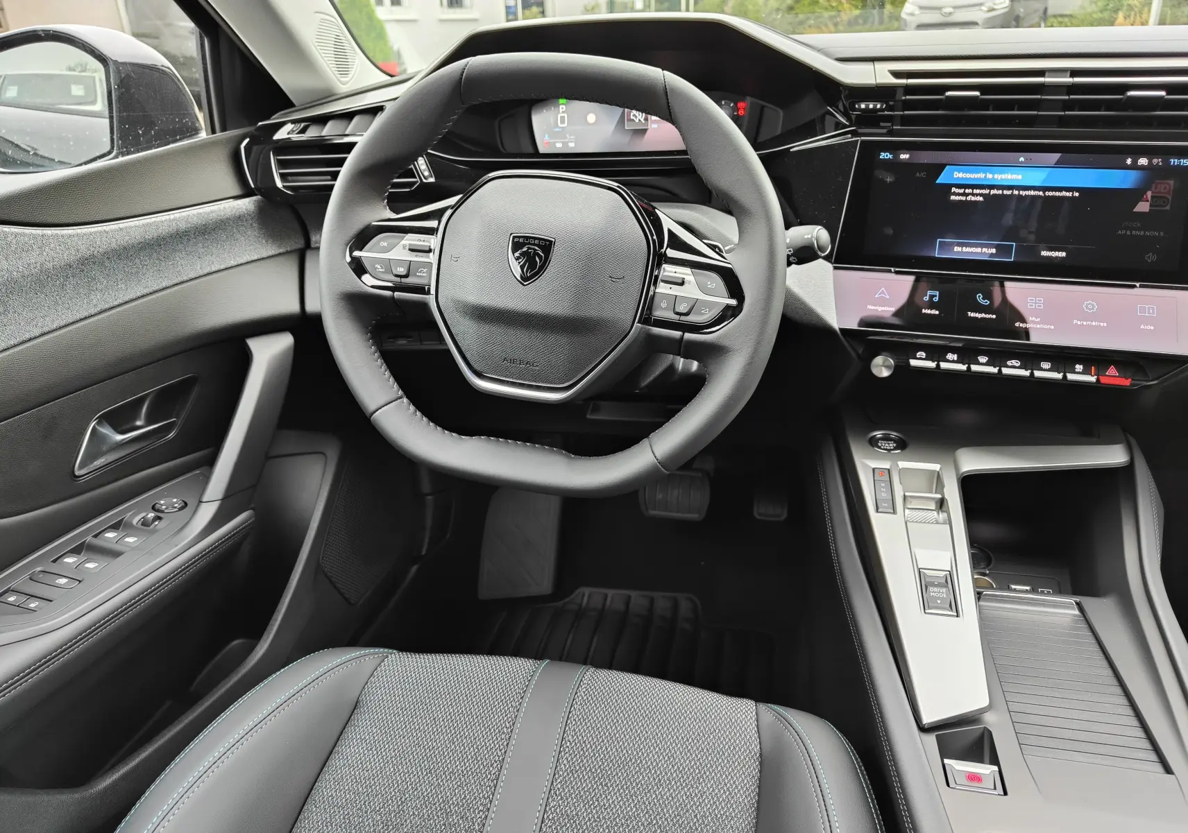 Vue intérieure centrée sur le volant compact et la console centrale moderne de la Peugeot 308 PureTech 130 Allure Pack noire 2023.