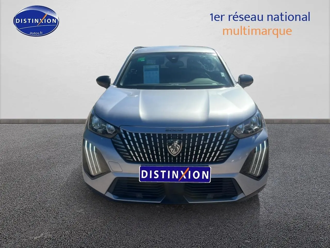 Vue frontale d'un Peugeot 2008 gris artense 2025 avec calandre distinctive et feux LED verticaux allumés.